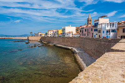 Buildings by sea against cloudy sky