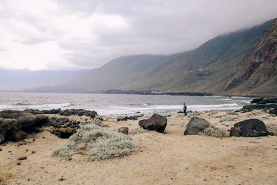 Scenic view of sea and mountains against sky with a man's figure