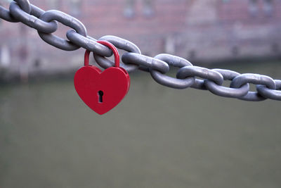 Close-up of heart shape padlock hanging from chain against river in city