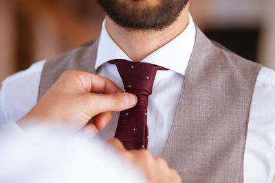 Cropped hands of man adjusting bridegroom necktie at wedding