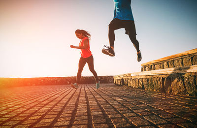 Couple running on promenade against clear sky during sunset