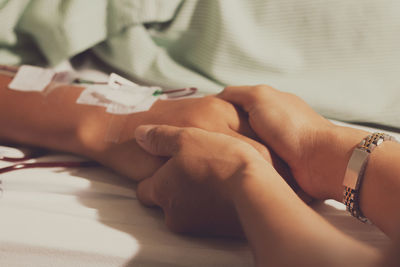 Close-up of woman holding patient hand lying on bed at hospital