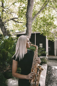 Woman playing saxophone against tree
