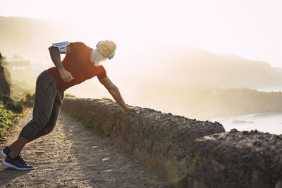 Senior man exercising on mountain against sky