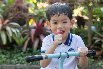 Boy eating lollipop while holding bicycle on footpath