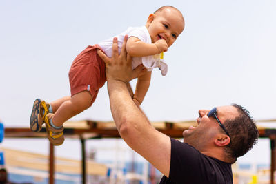 Low angle view of father holding baby against sky