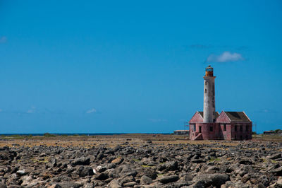 Lighthouse by sea against clear blue sky