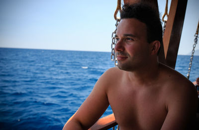 Shirtless young man looking away while sitting on boat at sea