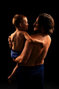 Rear view of shirtless man standing against black background