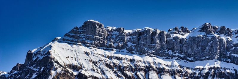 Low angle view of snowcapped mountains against clear blue sky