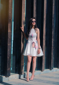 Full length of woman wearing sunglasses standing by wall