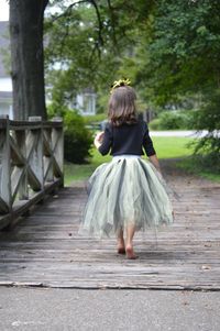 Rear view of girl wearing tutu walking on boardwalk at park