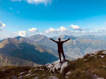 Rear view of man with arms outstretched standing on mountain against sky