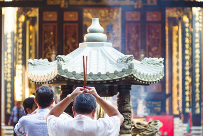 Rear view of man holding incenses at chinese temple