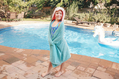 Girl wrapped in beach towel standing by pool. summer outdoor water activity for kids.