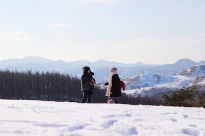 Women standing on snow at mountain peak against sky