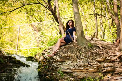 Portrait of young woman sitting on rock in forest