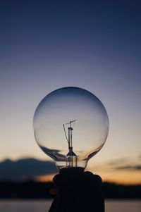 Close-up of illuminated light bulb against sky during sunset