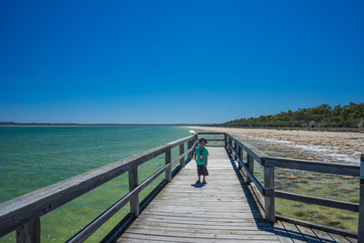 Rear view of man standing on railing against sea
