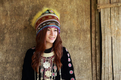 Smiling woman in traditional clothing standing by wooden wall