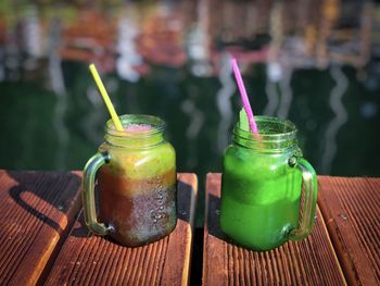 Two jars with colorful drinks on a wooden pontoon near the lake