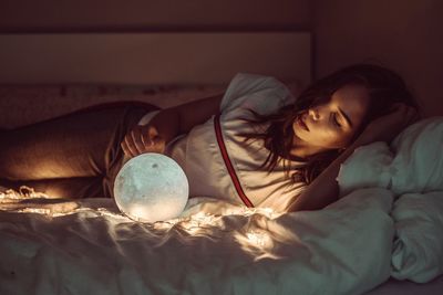 Woman sleeping with sphere and fairy lights on bed at home