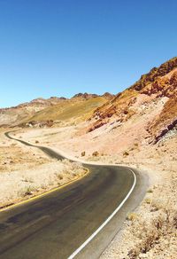 Scenic view of road by mountains against clear blue sky