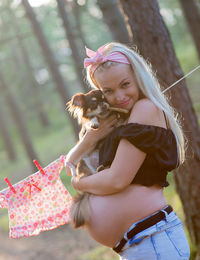 Portrait of beautiful pregnant woman standing while embracing dog