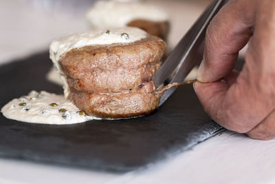 Close up on a masculine hand cutting a twine of a tenderloin with green pepper.