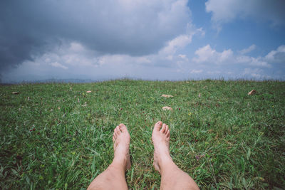 Low section of person sitting on field against sky