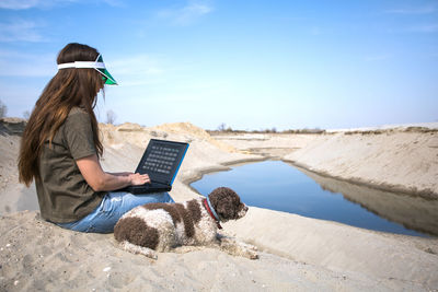 Rear view of woman using laptop while sitting on sand at beach