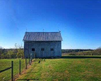 Barn on field against clear blue sky