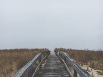 Boardwalk on field against clear sky