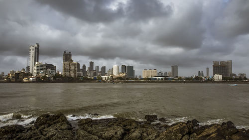 City at waterfront against cloudy sky