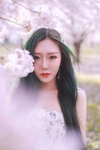 Portrait of a beautiful young woman standing against pink flowering plants