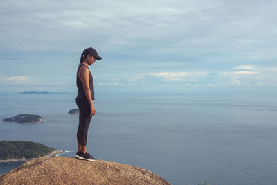 Side view of woman standing on rock against sea