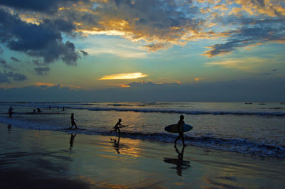 Silhouette people standing on beach against sky during sunset