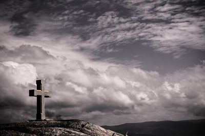 Cross on cliff against cloudy sky