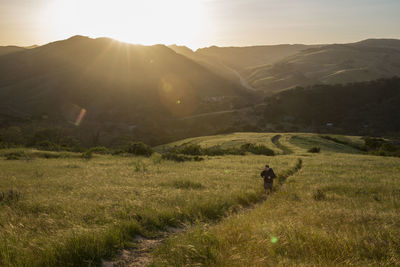 High angle view of man on trail amidst grassy field against mountains during sunset