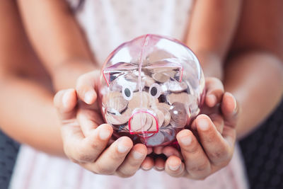 Midsection of mother and daughter holding piggy bank