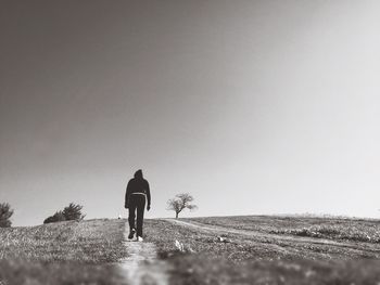 Rear view of one person walking on field against clear sky