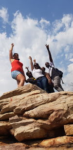 Low angle view of friends enjoying on rock against sky