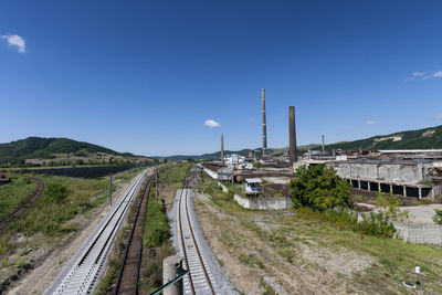 Railroad tracks by factory against blue sky