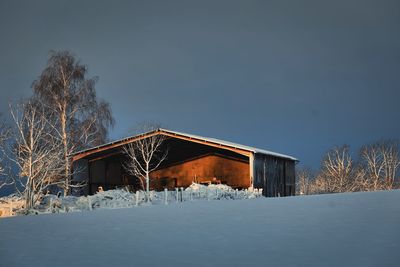 Farming building in snow covered field against sky