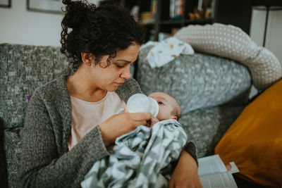 Mother feeding baby boy while sitting at home