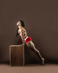 Side view full length of athlete exercising against brown background