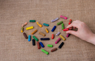Cropped hand making heart shape with colorful crayons on table