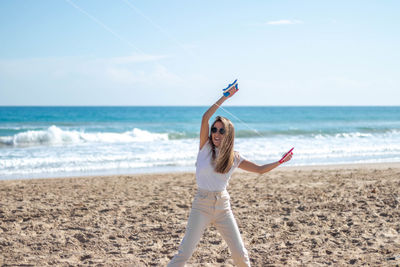 Portrait of happy, smiling young woman flying a kite on the beach on a sunny day