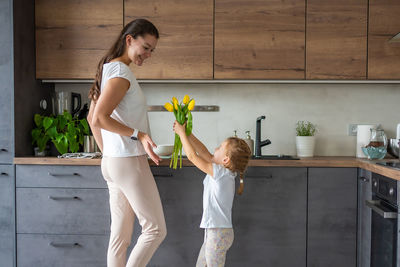 Side view of young woman with arms raised standing at home