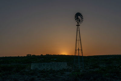 Silhouette wind turbines on field against sky during sunset